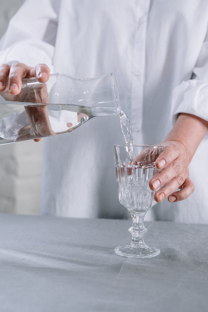Close-up of hands pouring water from a jug into a crystal glass on a table.